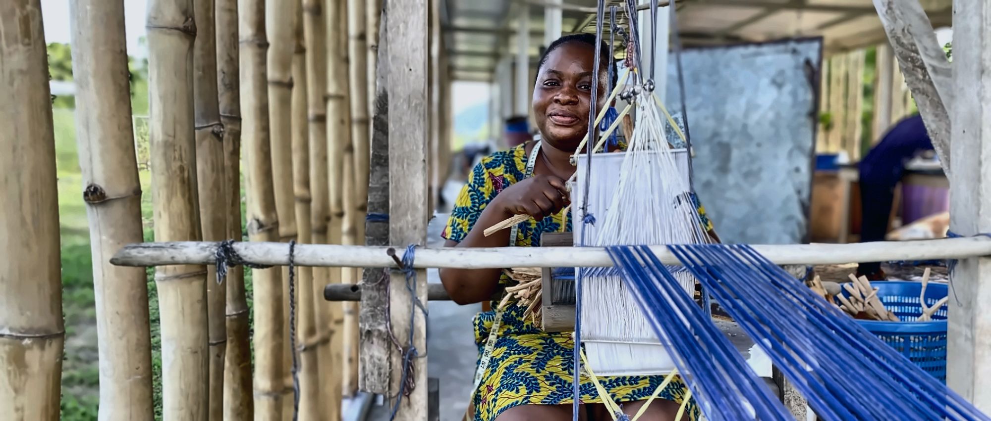 A weaver at a loom under a bamboo shelter